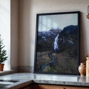 May include: A framed photograph of a waterfall cascading down a mountainside. The photo is in a black frame and is hanging on a wall in a kitchen.
