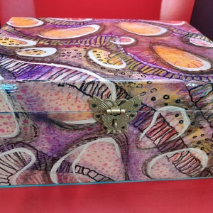 May include: A wooden box with a colorful abstract design featuring swirls, dots, and lines in shades of purple, pink, orange, and yellow. The box has a metal butterfly-shaped latch.