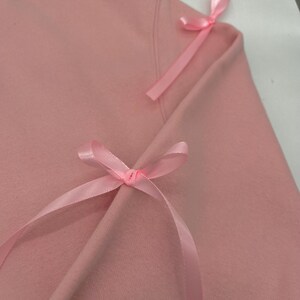 May include: A pink sweatshirt with two pink satin bows tied on the shoulders.