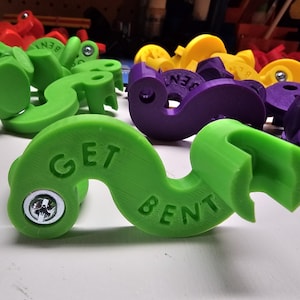 May include: A green plastic object shaped like a question mark with the words "GET BENT" printed on it. The object has a screw in the center of the top.