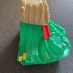 May include: Green and white plastic toy mountain with a red bridge and a yellow track. The mountain has a small, white, plastic fence around the top. The toy is made by Little Tikes.