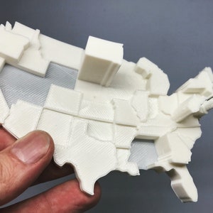 Può includere: Un modello in 3D stampato in bianco degli Stati Uniti d'America, con ogni stato rappresentato da un pezzo separato. Il modello è dettagliato e mostra i confini di ogni stato.