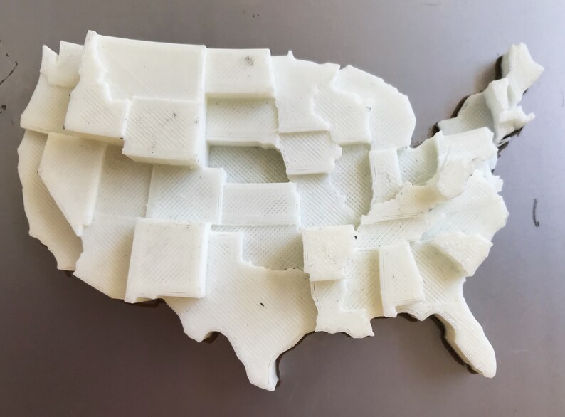 May include: A white 3D printed map of the United States, with each state outlined and raised.