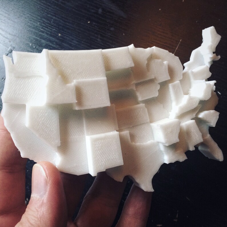 May include: A white 3D printed model of the United States of America, with each state represented as a separate block.