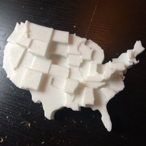 May include: A white 3D printed model of the United States of America, with each state outlined and textured.