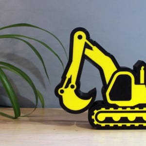Könnte beinhalten: Eine gelbe und schwarze 3D-gedruckte Baggerskulptur. Der Bagger befindet sich in einer Grabposition mit ausgefahrenem Arm und abgesenktem Löffel.