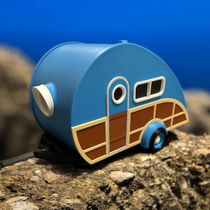 Op de afbeelding: Een blauwe en bruine speelgoedcamper met een witte deur en ramen. De camper heeft een witte ventilatieopening aan de zijkant en een bruine houten afwerking.