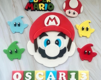 May include: A Super Mario themed cake topper set with a red and white Mario head, a red mushroom, a yellow star, and blue, green, and red stars. The set also includes a name banner with the name "OSCARI3" in colorful blocks.