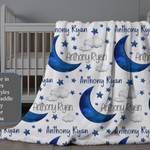 May include: A white baby blanket with a blue crescent moon and stars pattern. The blanket is personalized with the name "Anthony Ryan" repeated throughout the design.