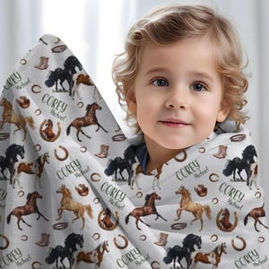 Pu&ograve; includere: Una coperta bianca a tema cavallo, con illustrazioni di cavalli marroni, neri e beige. La coperta include anche stivali da cowboy, ferri di cavallo e il nome "Corey Michael" ripetuto.