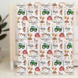 May include: White baby blanket with a repeating pattern of farm animals, tractors, and barns. The blanket features the text "MAXWELL JAMES" in a repeating pattern. The blanket is displayed on a white crib.