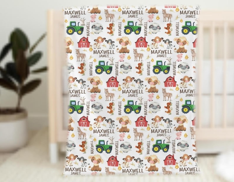 May include: White baby blanket with a repeating pattern of farm animals, tractors, and barns. The blanket features the text "MAXWELL JAMES" in a repeating pattern. The blanket is displayed on a white crib.