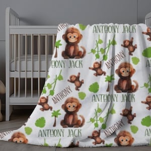 May include: White fleece blanket with a repeating pattern of brown monkeys and green leaves. The blanket has the name "Anthony Jack" printed on it multiple times.