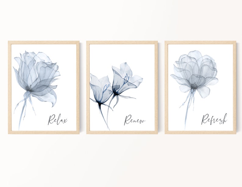 May include: Set of three framed floral art prints. Each print features a delicate, translucent blue flower against a white background. The words "Relax", "Renew", and "Refresh" are written in cursive below each flower. The frames are light brown.