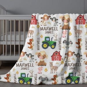 May include: White baby blanket with a farm animal pattern, including cows, pigs, and sheep. The blanket features a green tractor, red barn, and the name "MAXWELL JAMES" in black text. The blanket is draped over a white crib.
