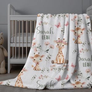 May include: White baby blanket with a floral and giraffe print. The blanket features the names "Sarah Leah" repeated throughout the design.
