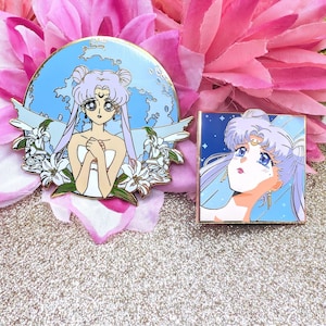 Puede incluir: Dos pines de esmalte con ilustraciones de estilo anime. Uno es circular con un fondo azul y un personaje con cabello lavanda, rodeado de flores blancas. El otro es cuadrado con un fondo azul estrellado y un personaje con cabello lavanda.