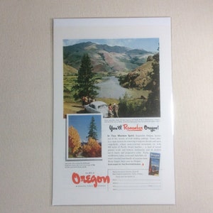 以下が含まれることがあります： オレゴン州のヴィンテージ旅行広告。川、山、クラシックカーのある美しい風景が特徴です。「You'll Remember Oregon!」というテキストと、小さな風景画像が含まれています。