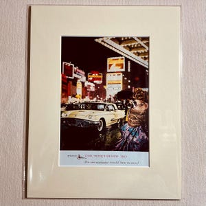 May include: A framed print of a cream-coloured Ford Thunderbird '59, with a white top, in a city scene. The image includes the text "Ford Thunderbird '59 The car everyone would love to own!" The car is parked on a wet street.