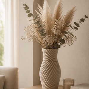 Könnte beinhalten: Eine matte, cremeweiße Keramikvase mit einer spiralförmigen, gerippten Textur. Die Vase ist mit einem Trockenblumenarrangement gefüllt, das aus hohem, federartigem Pampasgras, zartem weißem Schleierkraut und grünen Eukalyptuszweigen besteht.