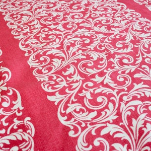 May include: Red table runner with a white, ornate, scrolling floral pattern. The runner has a textured appearance and a repeating design. The edges feature a similar, but narrower, border design. This runner is suitable for home decor.