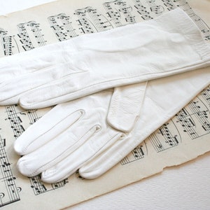 May include: A pair of white leather gloves on a sheet of music. The gloves are long and have a simple design.