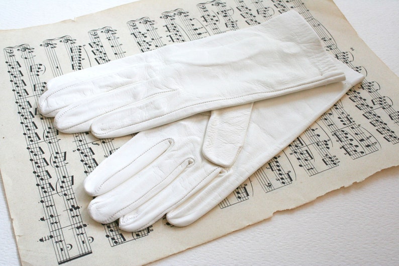 May include: A pair of white leather gloves on a sheet of music. The gloves are long and have a simple design.