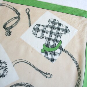 May include: A cream-colored fabric with a green border. The fabric features a black and white plaid design of a dog, a collar, and a leash.