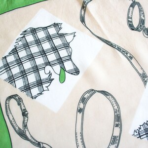May include: A white cotton handkerchief with a green border. The handkerchief features a black and white plaid design of a dog with a green collar and leash. The handkerchief also has a black and white plaid design of a dog collar.