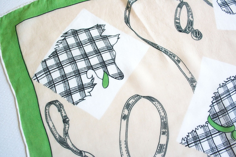 May include: A white cotton handkerchief with a green border. The handkerchief features a black and white plaid design of a dog with a green collar and leash. The handkerchief also has a black and white plaid design of a dog collar.