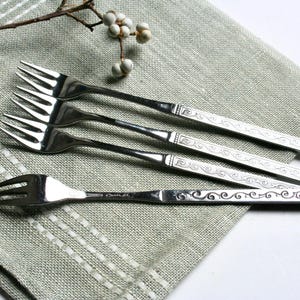 May include: Four silver forks with ornate designs on a light green linen napkin.
