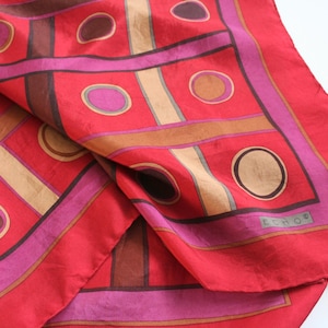 Puede incluir: Un pañuelo de seda rojo con un patrón geométrico de círculos y cuadrados marrones, beige y rosas. El pañuelo tiene la palabra "Echo" impresa en blanco en la esquina inferior derecha.