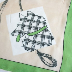 May include: A white and green patterned scarf with a black and white illustration of a dog wearing a green collar. The scarf has a green border.