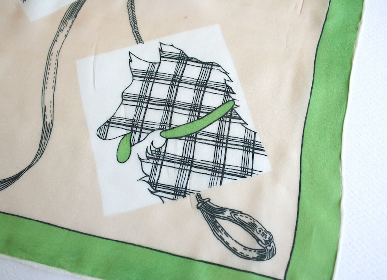 May include: A white and green patterned scarf with a black and white illustration of a dog wearing a green collar. The scarf has a green border.