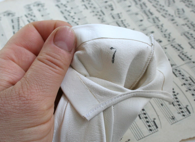 May include: White leather gloves with a number 7 written on the inside of the glove.