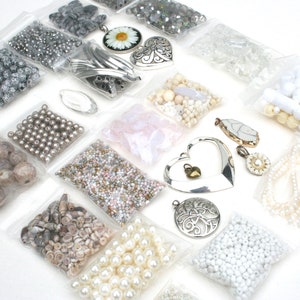 May include: Assortment of jewelry-making supplies, including beads, pendants, and charms, packaged in clear plastic bags. The beads vary in color and material, with silver, pearl, and iridescent options. Several heart-shaped pendants and a daisy pendant are also visible.