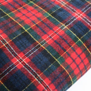 May include: A fabric featuring a classic tartan plaid pattern with intersecting lines in vibrant red, deep navy blue, and dark forest green. The textile has a soft, slightly fuzzy texture with thin white and yellow accent stripes throughout the design.