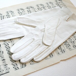 May include: A pair of white leather gloves with a simple design. The gloves are laid out on a sheet of music.