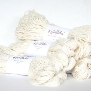 May include: Cream-colored yarn skeins and bundles. The image shows several skeins of yarn, some bundled and others loose, with labels that read "Knit Picks". The yarn appears to be a soft, natural fiber, perfect for knitting or crocheting projects.