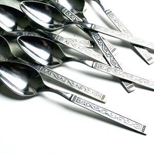 May include: A set of silver spoons with an ornate design. The spoons are arranged in a pile on a white surface.