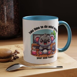 May include: White ceramic mug with a blue interior and handle. The mug features a cartoon koala playing a video game, with the text "Take time to do what makes your soul happy."