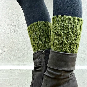 Puede incluir: Botas grises de ante con tacón y cremallera, combinadas con calentadores de piernas de punto verdes. Los calentadores de piernas tienen un diseño de punto trenzado. El texto "Original Design by Britta Graham © 2015" es visible.