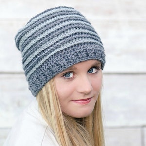 May include: A gray and light blue striped crochet beanie hat. The hat is made with a soft yarn and has a slouchy fit.