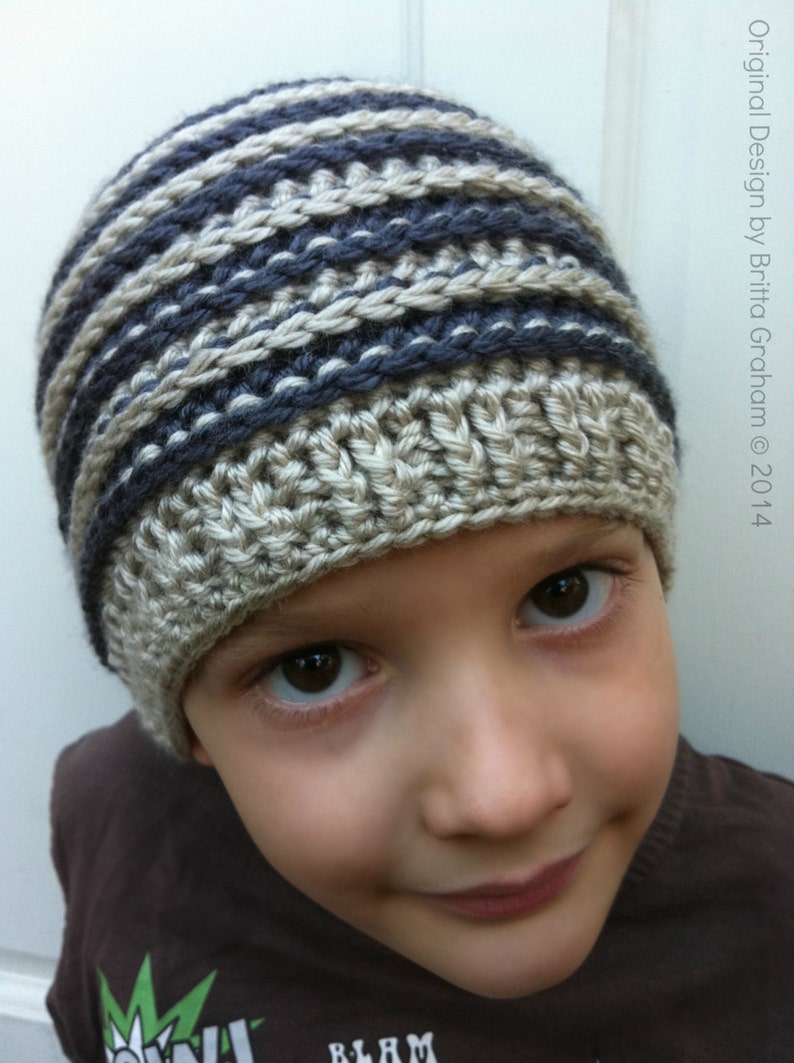 May include: A young person wearing a striped crocheted hat in shades of gray and beige. The hat has a simple design and is made with a soft yarn.