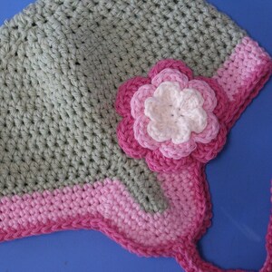 May include: A crocheted hat with a pink flower and a pink and green trim. The hat has a long pink tie.