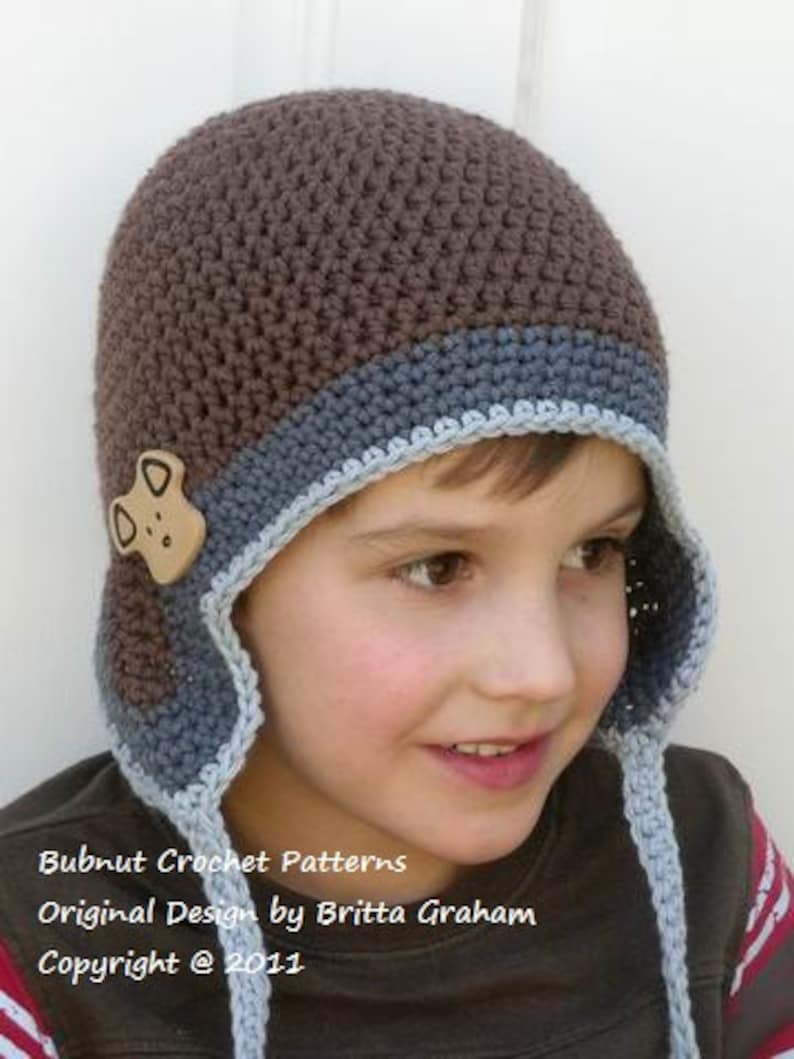 May include: A brown and blue crocheted hat with a brown felt dog applique. The hat has a long, blue crocheted tie. Bubnut Crochet Patterns Original Design by Britta Graham Copyright &copy; 2011