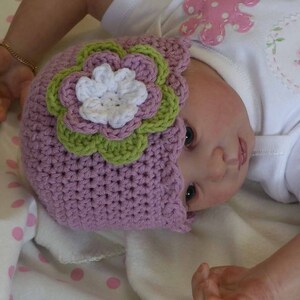 May include: A purple crocheted baby hat with a green and white flower design.