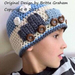 May include: A blue, white, and gray crocheted hat with brown buttons shaped like car wheels. The hat is worn by a child with a striped shirt.