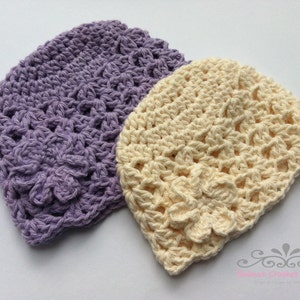May include: Two crocheted hats, one in a light purple color and the other in a cream color. Both hats have a delicate, lacy pattern.