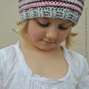 May include: A young girl wearing a gray and pink striped knitted hat. The hat has a simple design with alternating stripes of gray and pink yarn.